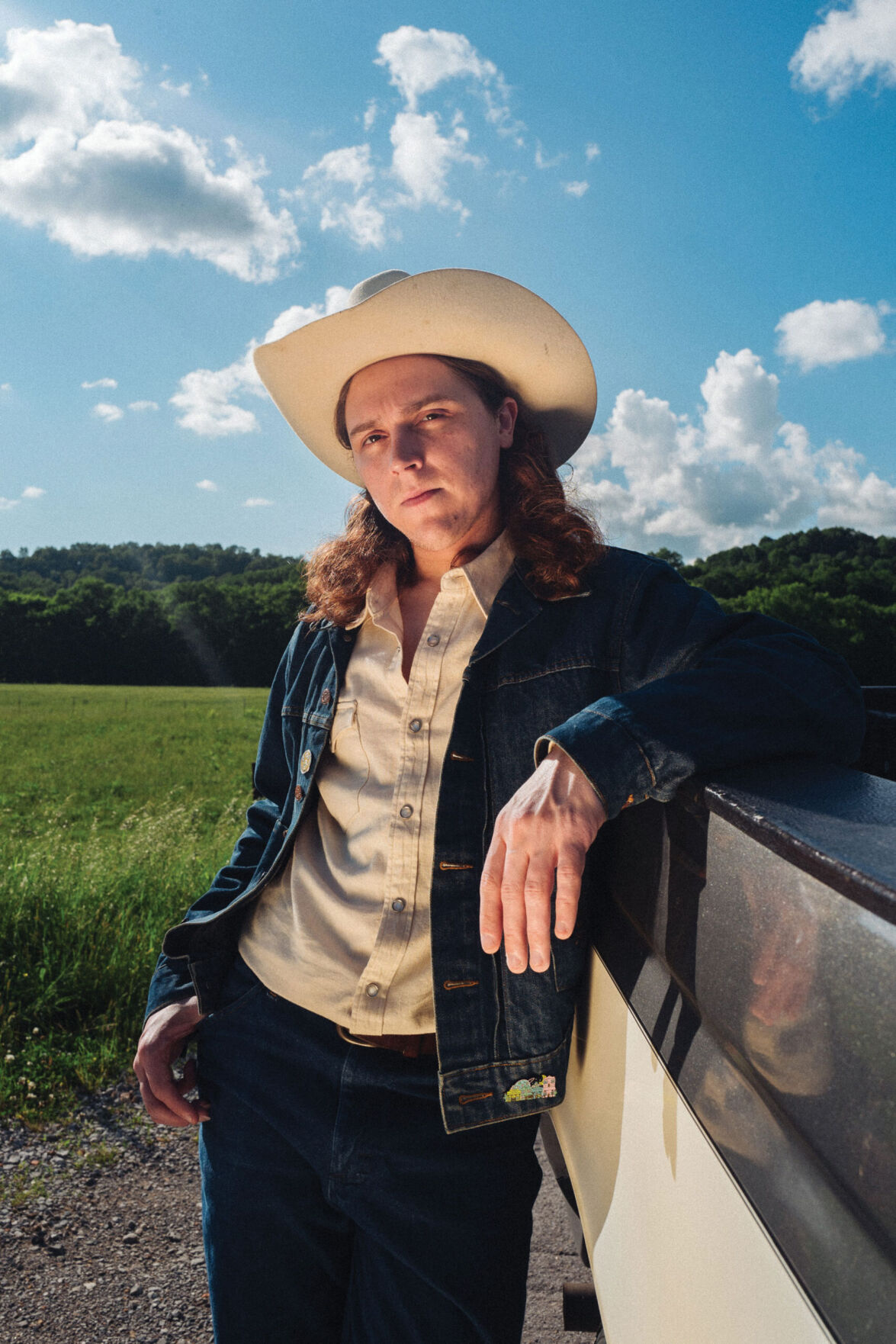 Daniel Donato press photo 2025 artist leans against the side of a pickup next to a field